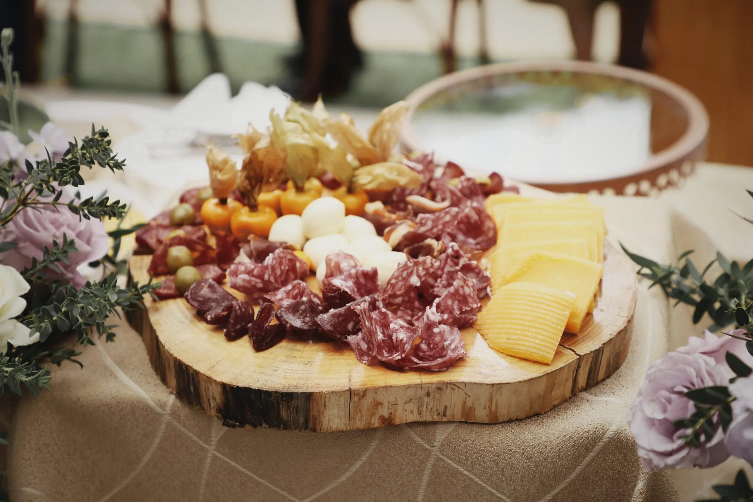 A wooden board of charcuterie and cheese among flowers.