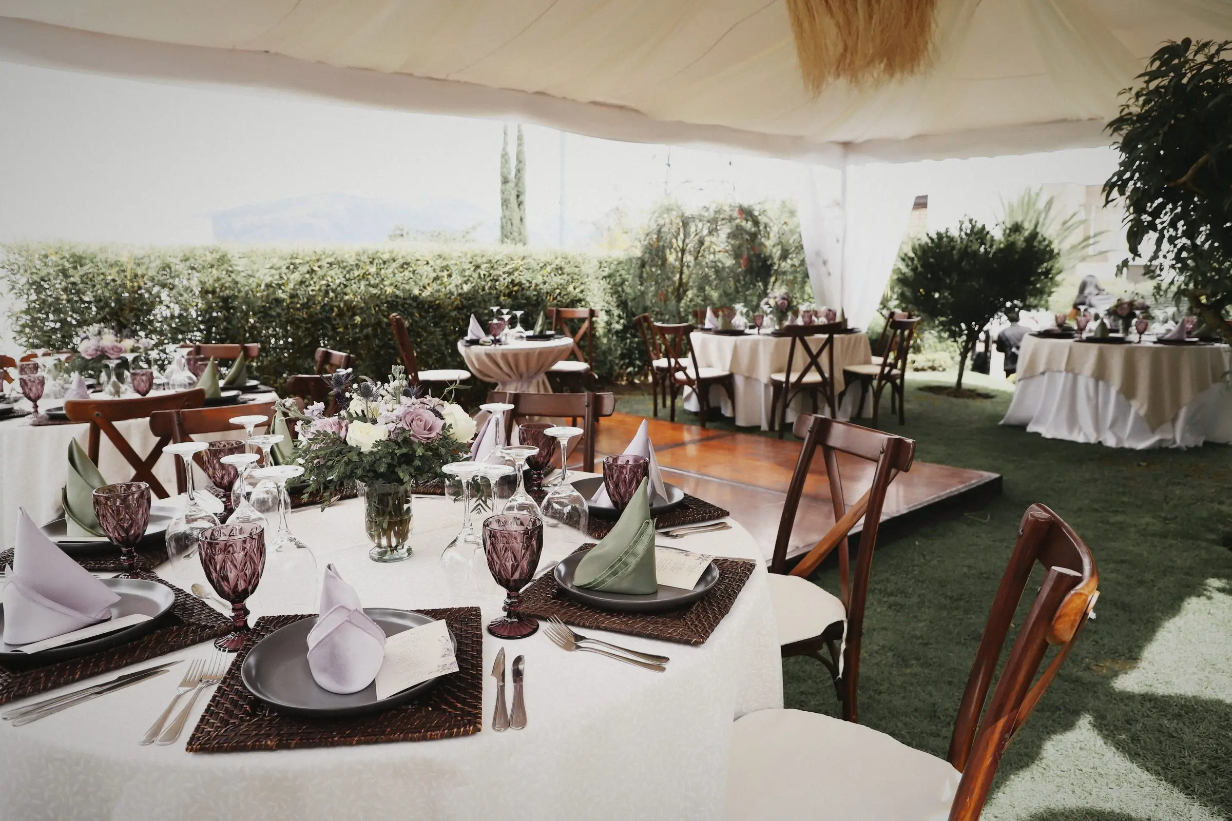 A garden reception under a white canopy: set tables, glassware and flowers before the guests arrive.