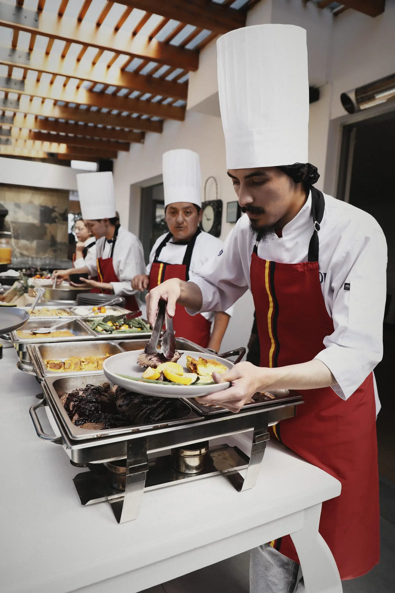 A cook plating food from chafing dishes at the line.